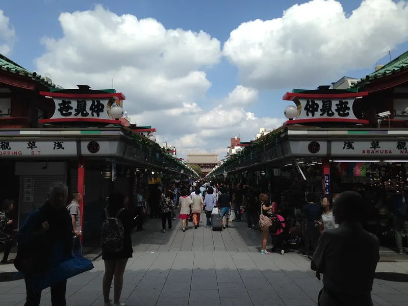 Nakamise street between rows of shops, with visitors seen from behind and the Hozomon Gate in the distance under a blue sky