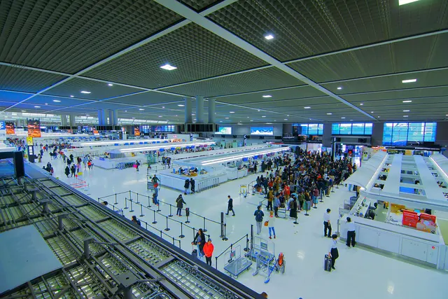 A departure lobby seen from above with check-in islands and queues of passengers under a grid ceiling