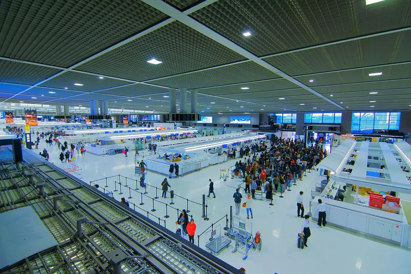 A departure lobby seen from above with check-in islands and queues of passengers under a grid ceiling