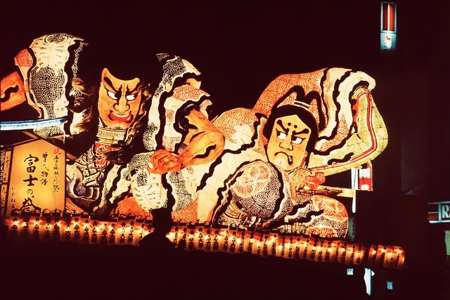 An illuminated paper float of two fierce warrior figures at night