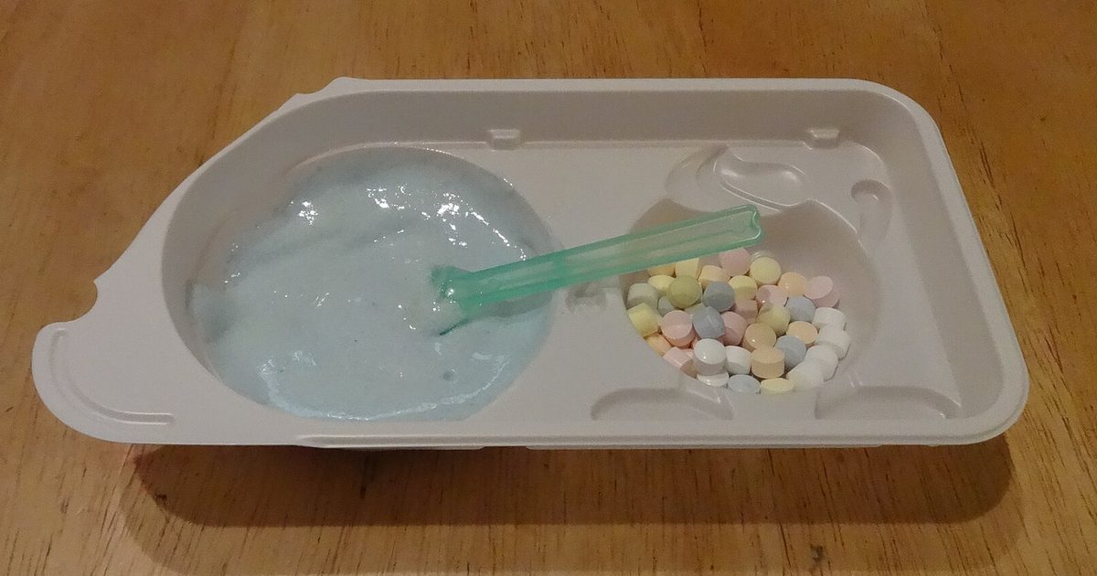 A beige plastic tray on a wooden table, with pale blue foam and a green spoon in one hollow and small pastel candy pieces in the other