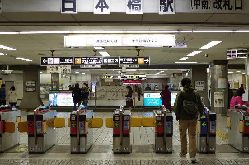 Ticket gates at Nippombashi Station on the Osaka Metro, with overhead signs pointing to the Sakaisuji and Sennichimae line platforms