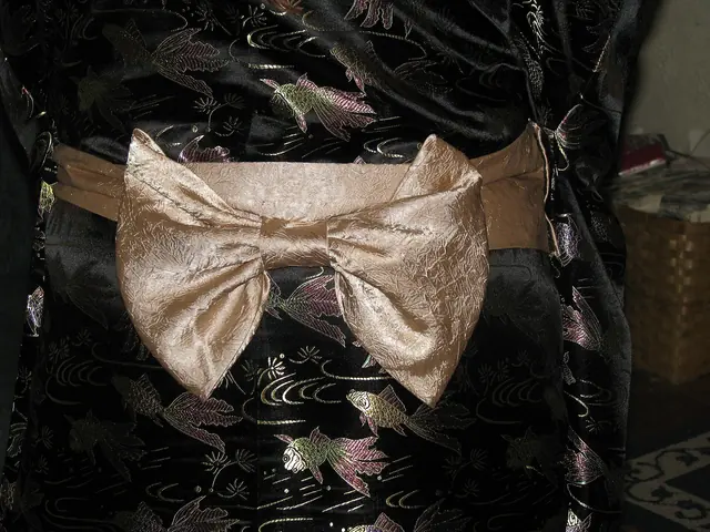 Close-up of a pale gold obi bow on the back of a black kimono patterned with goldfish