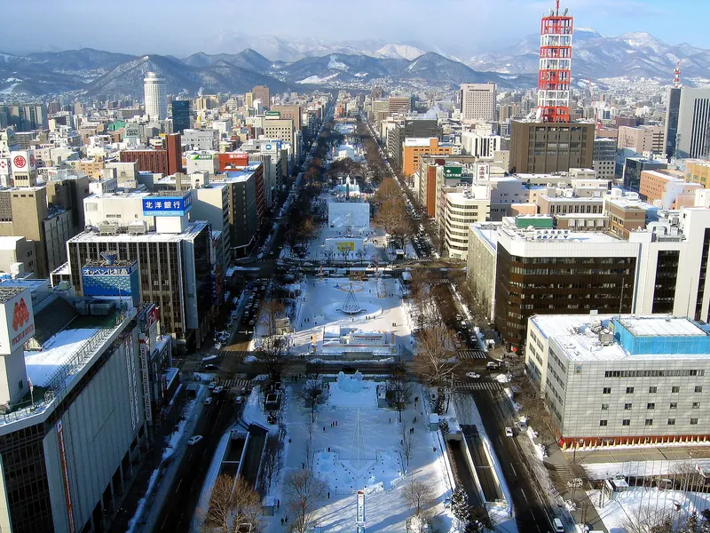 Odori Park under snow seen from above with the red TV tower on the right and snowy mountains beyond