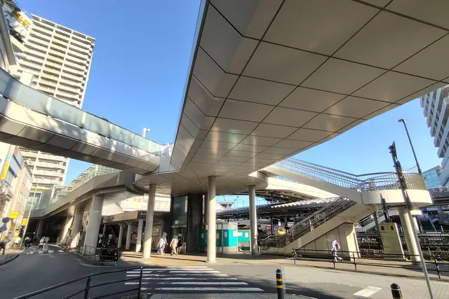 The underside of a raised pedestrian deck on round columns, seen from the street, with a staircase on the right and a tall apartment block on the left