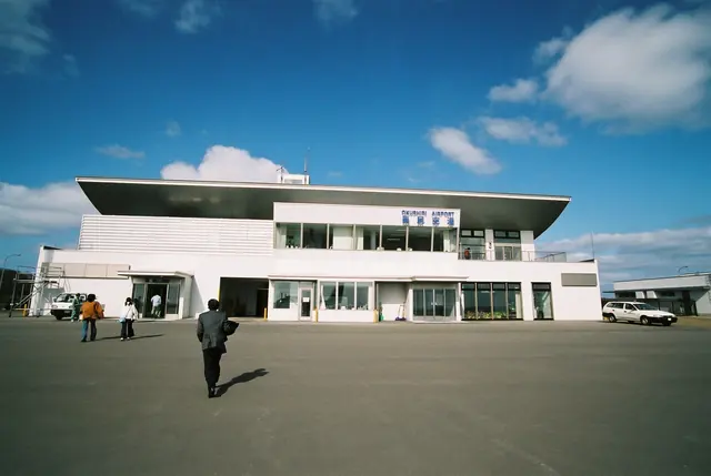 A low white terminal building with a wide flat roof seen across the apron, with a few people walking towards it