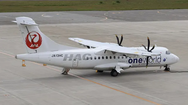 A white twin-propeller aircraft with a red crane emblem on its tail standing on an airport apron