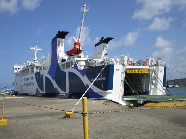 A white and blue ferry moored at a quay with its side ramp open, with a yellow bollard and a mooring rope in the foreground