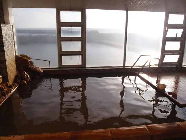 A bath filled with brown hot-spring water below large steamed-up windows, with a handrail leading into the water