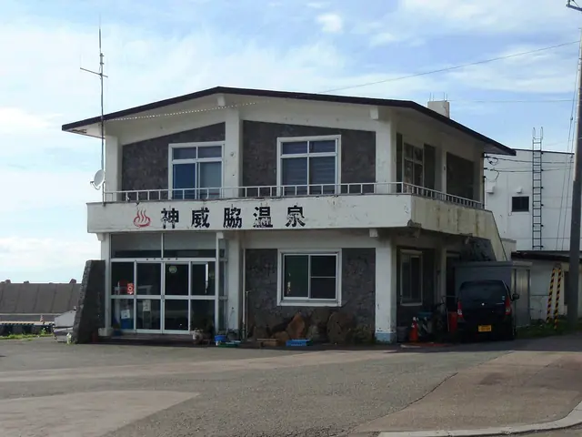 A two-storey building with a balcony and a sign reading Kamuiwaki Onsen in Japanese above its entrance