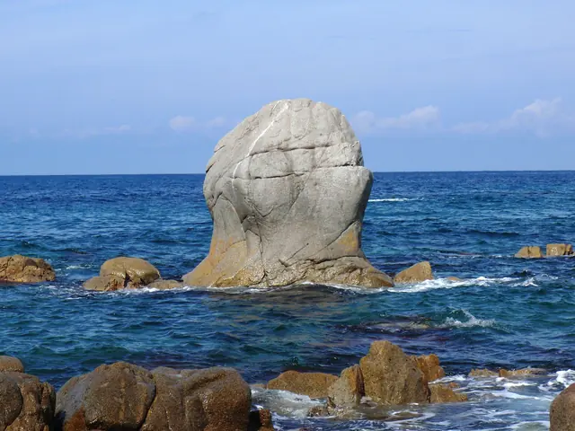 A pale, rounded rock standing in deep blue surf among smaller brown rocks
