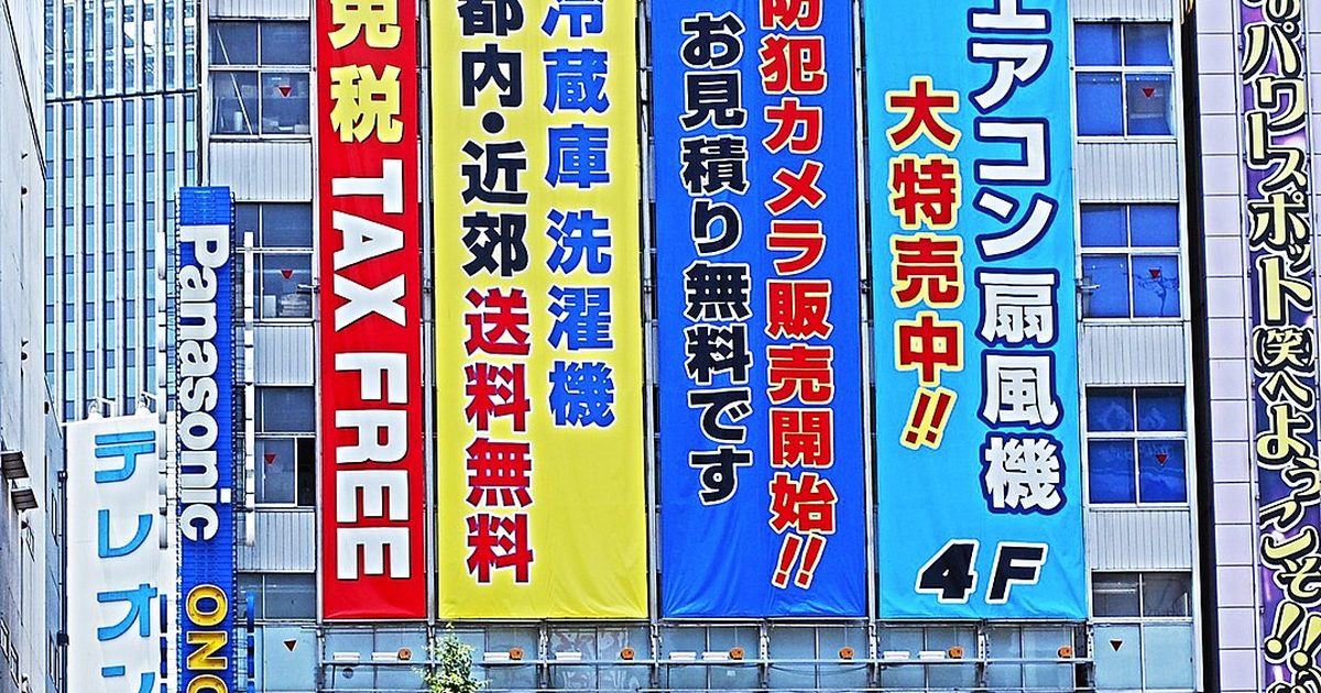 A shopfront covered in tall red, yellow and blue banners, one reading TAX FREE, above a yellow strip reading TAX FREE in English and Japanese, with a vertical ONODEN sign at the left