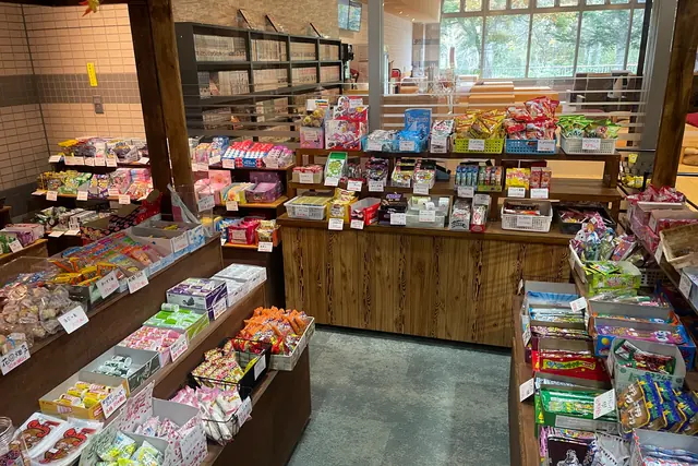 Wooden counters covered in baskets and boxes of colourful small sweets with handwritten price tags, with shelves of comic books and large lounge windows behind