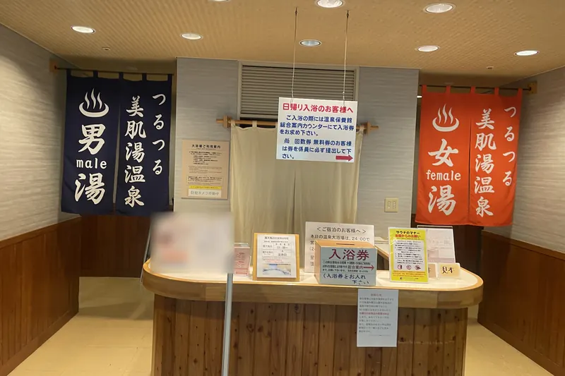 A counter with a box for bathing tickets between two doorways hung with split curtains, a navy one marked male on the left and an orange one marked female on the right