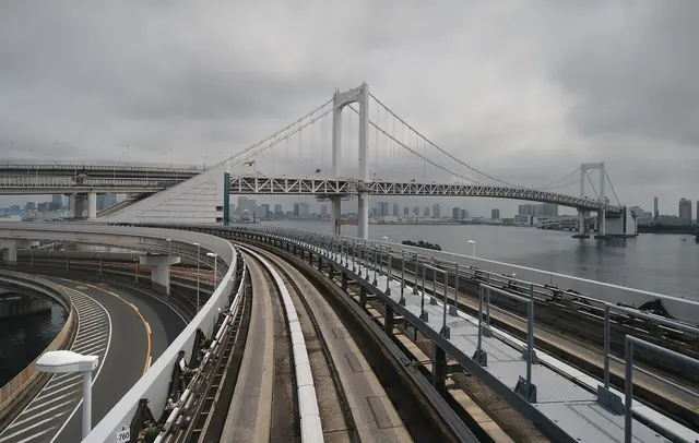 A suspension bridge under an overcast sky, with an elevated guideway curving towards it