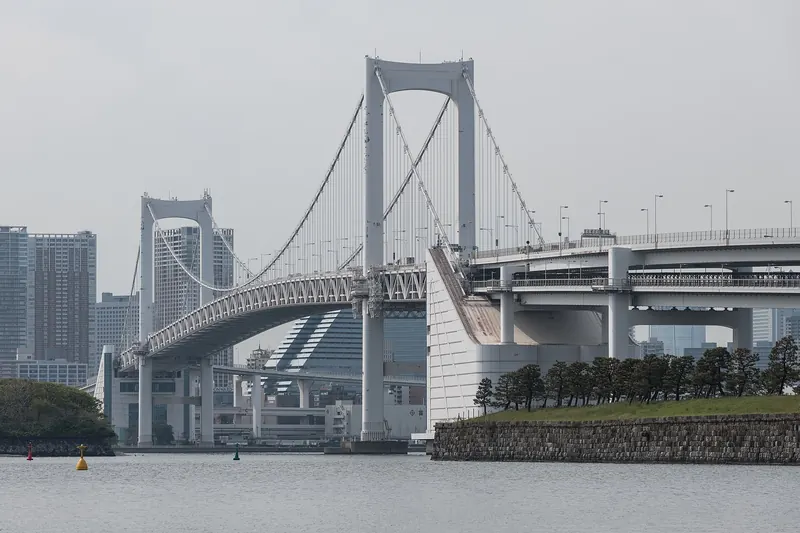 Two white towers, main cables and the two-level deck of a suspension bridge under a grey sky
