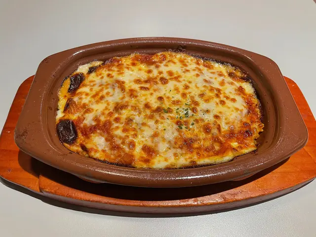 Baked rice with melted cheese in an oval brown dish on a wooden board