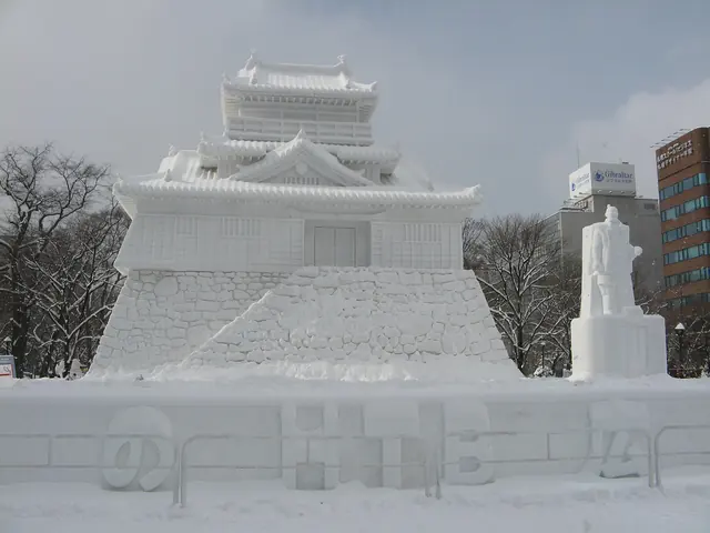 A large snow sculpture of a Japanese castle with city buildings behind under a grey sky