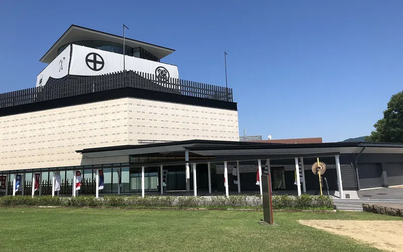 A pale museum building with a black-and-white top storey marked with clan crests under a blue sky