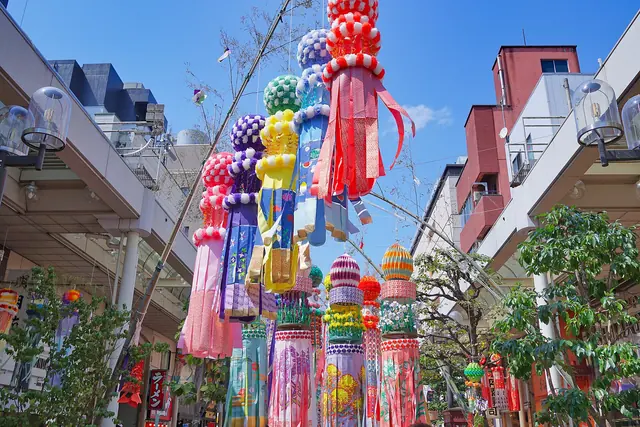 Colourful paper streamers hanging from bamboo above a shopping street under a blue sky