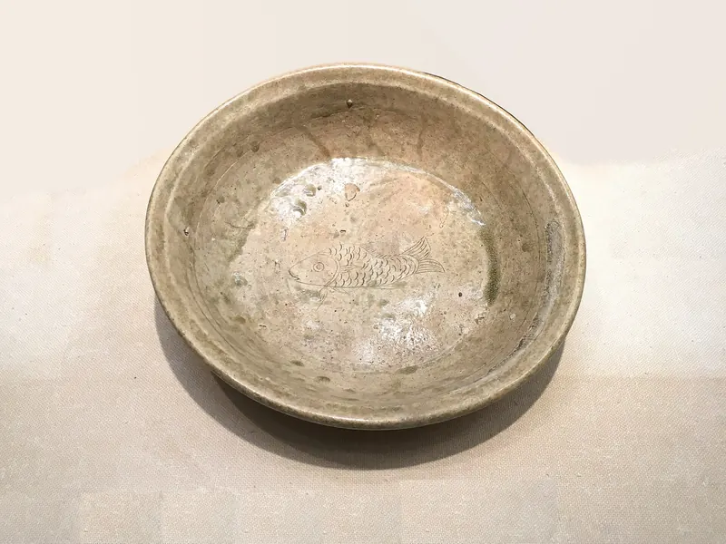 A shallow pale green-grey basin with a faint fish design scratched into the bottom