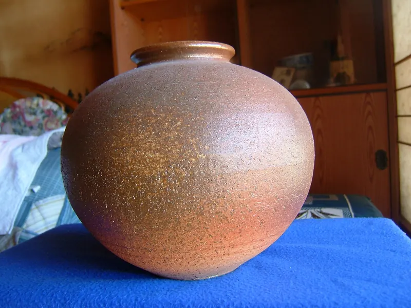 A large round jar with a rough orange-brown surface flecked with small white grains, on a blue cloth