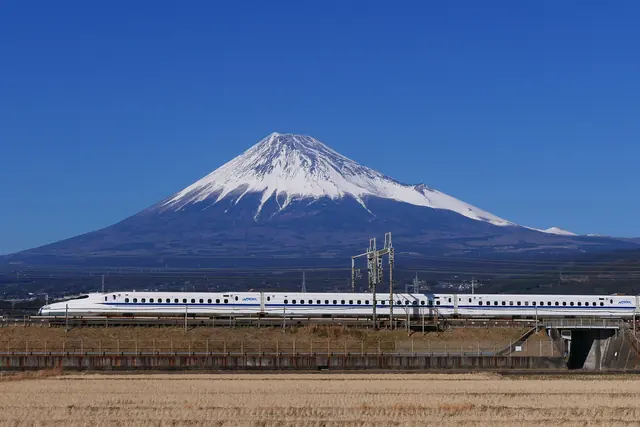 A white Shinkansen passing in front of snow-capped Mount Fuji under a deep blue sky