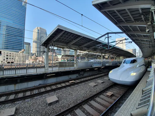 The white nose of a Shinkansen at a Tokyo Station platform with office towers behind