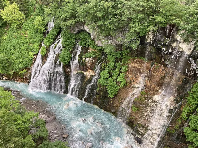 Water running down a rock face into the pale-blue Biei River
