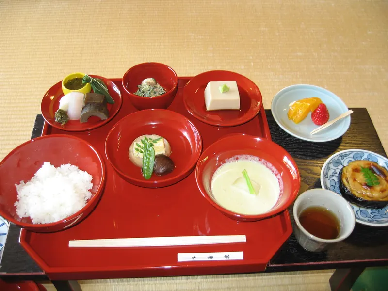 A red lacquer tray of small vegetarian dishes in red bowls, with a bowl of rice, a cup of tea and a plate of fruit