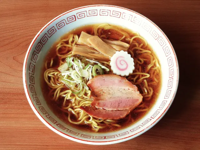 A bowl of soy-sauce ramen with pork, bamboo shoots, fish cake and spring onion seen from above