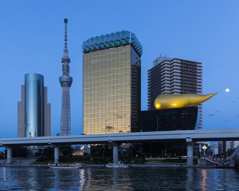 Tokyo Skytree with the golden Asahi Breweries building and the Asahi Flame at blue hour across the Sumida River