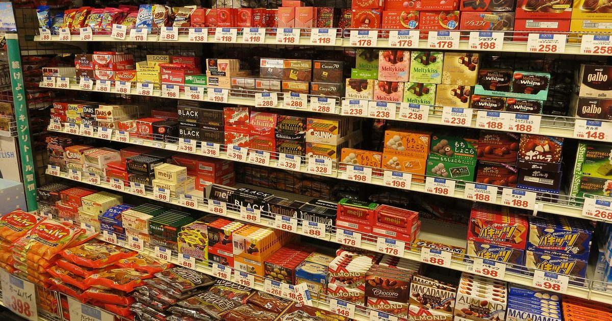 Shop shelves stacked with boxes and bags of chocolates and snacks, with yen price tags along each shelf edge