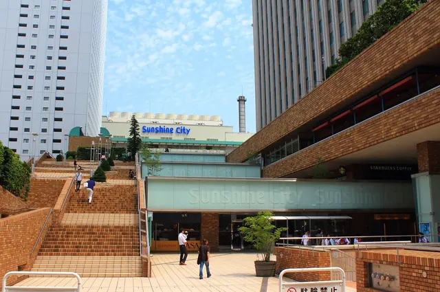 Brick steps leading up to a low building with a Sunshine City sign, with a tall white tower behind it