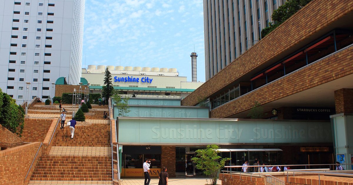 Brick steps leading up to a low building with a Sunshine City sign, with a tall white tower behind it