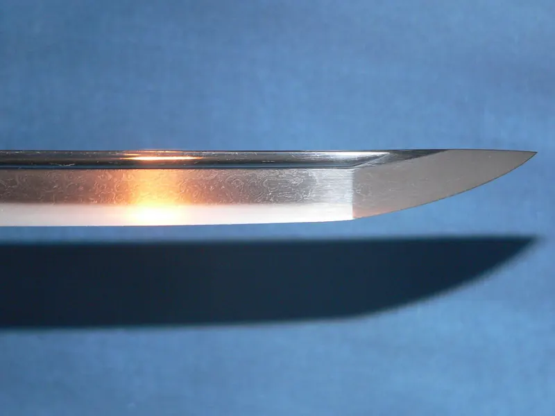The polished tip of a curved Japanese sword blade catching the light against a blue background