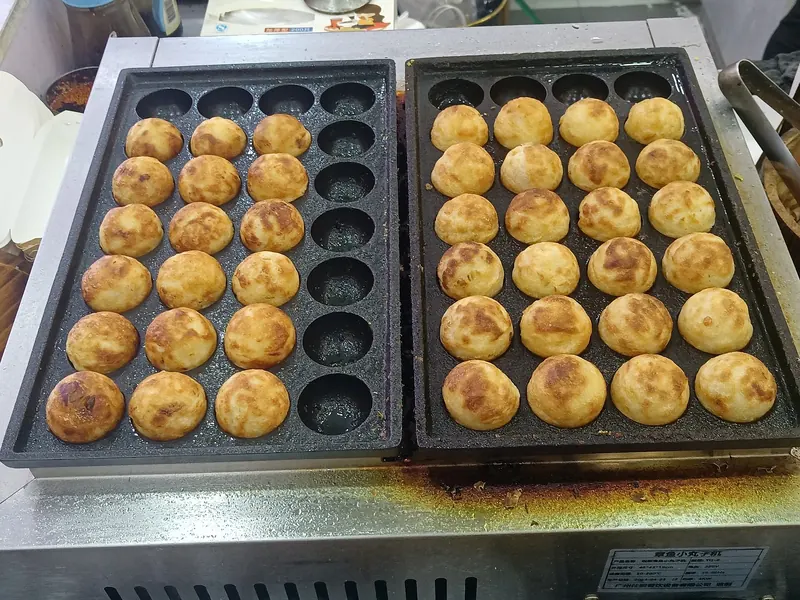 Two cast-iron pans with rows of golden takoyaki balls