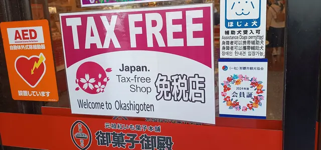 Photo: Naha Mama Pavilionz (CC0) A pink-and-white sign reading TAX FREE and Japan Tax-free Shop on a glass door