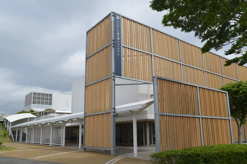 A museum entrance clad in vertical wooden slats beside a low white building under a grey sky