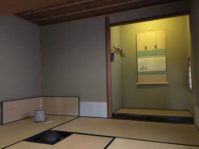 A small tatami tea room with a sunken hearth and kettle in the floor and a scroll hanging in the alcove