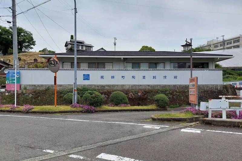 A low white building with a long sign on its wall, a lamp post and flower beds beside a road
