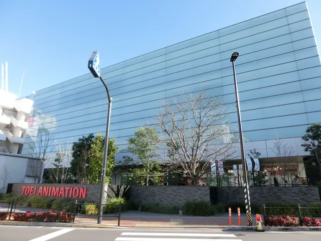 A large blue-green glass building behind a low wall with red Toei Animation lettering, with a street lamp and bare trees