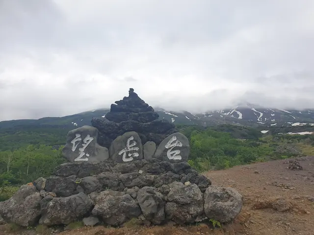 Stone cairn carved with the name of the Bogakudai lookout, with cloud over the mountain slopes behind