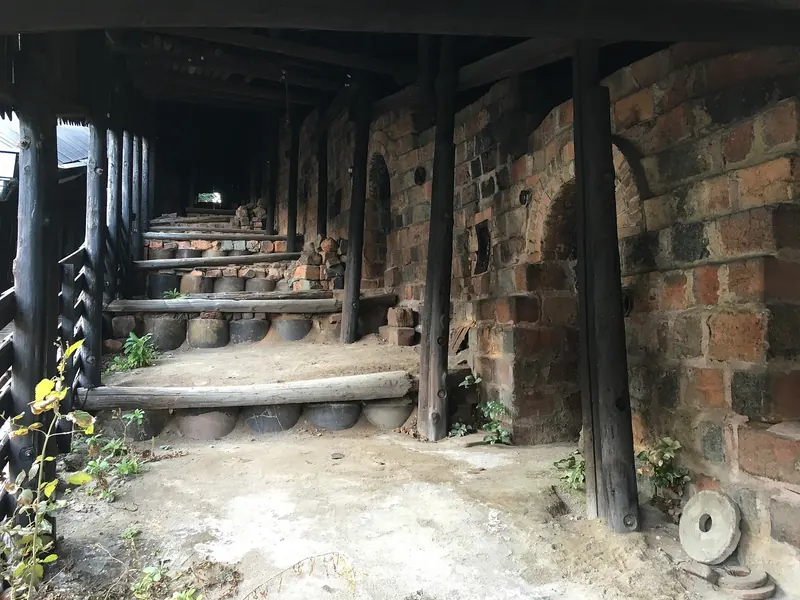 Inside a long covered kiln, with brick walls and arched openings stepping up a slope under a wooden roof