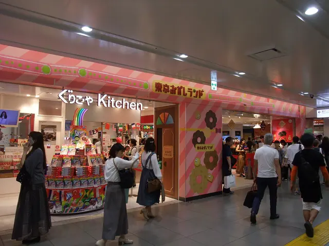 A pink shopfront decorated with doughnuts in an underground concourse, with shoppers at a stand of boxed snacks