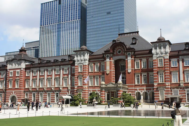 The red-brick Marunouchi building of Tokyo Station with glass towers behind it and a plaza and lawn in front