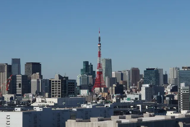 A red-and-white lattice tower standing among office towers by day