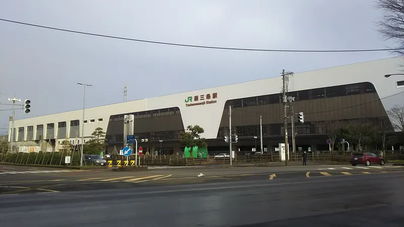 The long, low building of Tsubamesanjo Station with a green JR sign, across a wide road