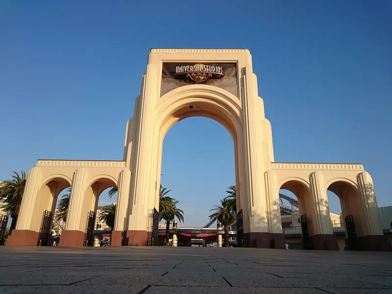 A large cream arch with Universal Studios lettering, flanked by palm trees under a blue sky