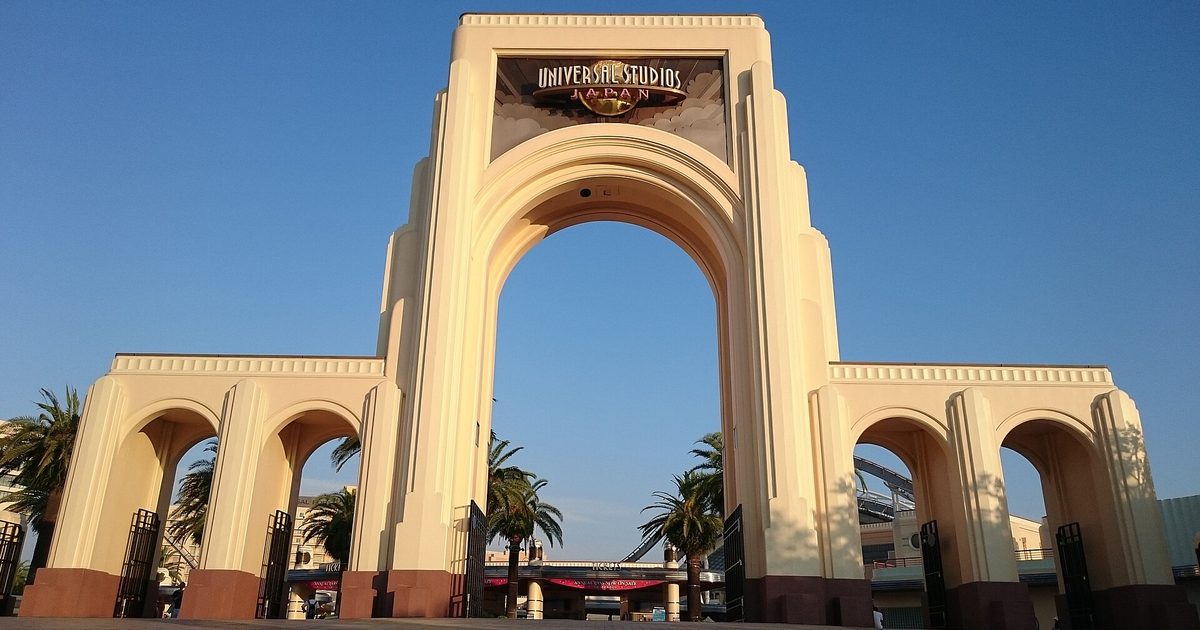 A large cream arch with Universal Studios lettering, flanked by palm trees under a blue sky